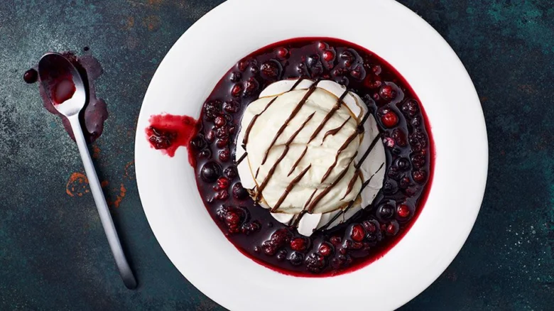 Dort pavlova s ovocem a čokoládou na bílém talíři.