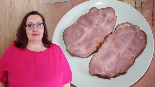 Žena stojí vedle talíře s dvěma plátky uzeného vepřového masa.