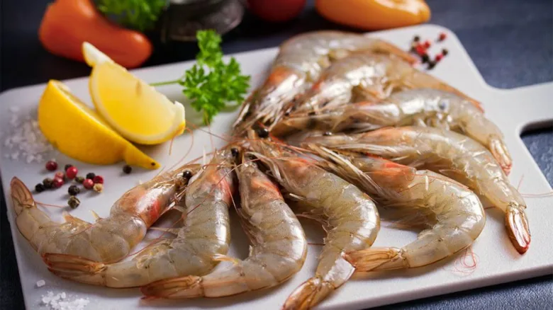 Surové krevety s citronem, petrželkou a pepřem na bílém talíři.