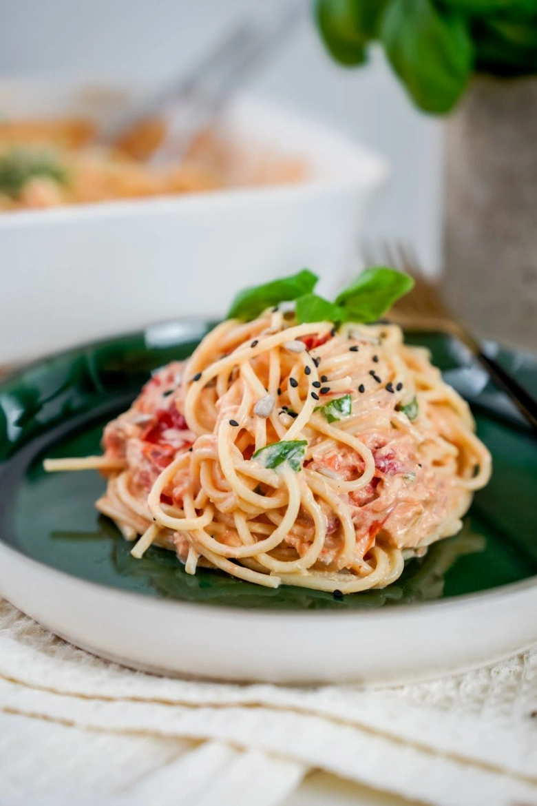 Pasta s lososem na talíři ozdobená bazalkou.