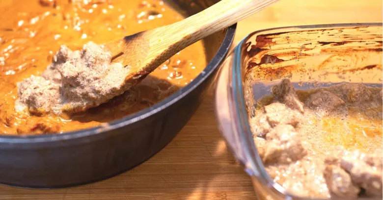 Převádění omáčky kuřecí tikka masala s kousky masa do skleněné misky.