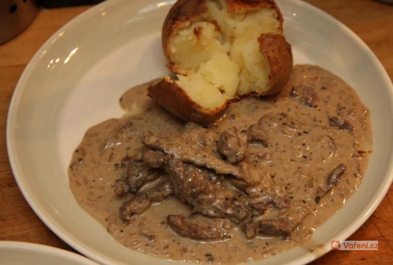 Steak s houbovou smetanovou omáčkou a pečeným bramborem na talíři.