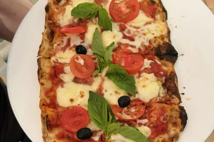 Pizzu s rajčaty, bazalkou a černými olivami na bílém talíři.