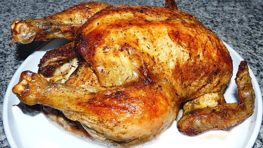 Zlatohnědá pečená celá kuřecí na bílém talíři.