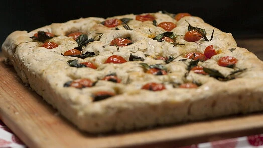 Focaccia s rajčaty a bylinkami na dřevěném prknu.