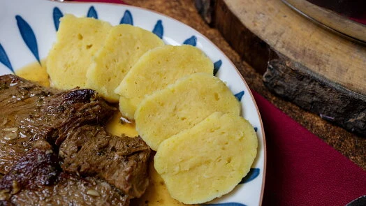 Domácí bramborové knedlíky podávané s masem na talíři.