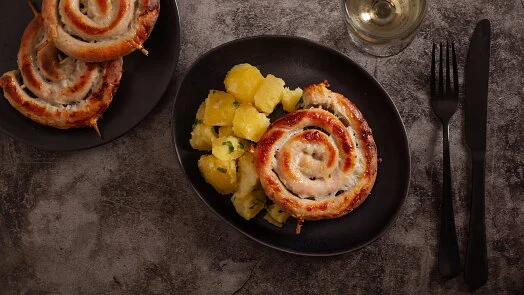 Pecené vinné klobásy ve spirále s bramborami na talíři.
