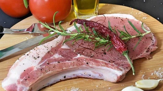 Surové vepřové kotlety s bylinkami a kořením na dřevěném talíři.