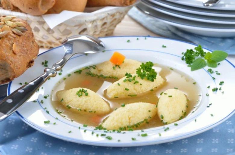 Polévka s knedlíky v misce posypanou česnekem a petrželkou.