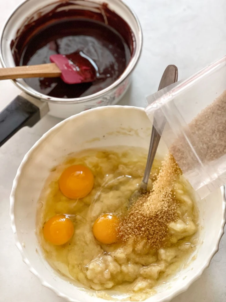 Příprava banánových brownies s vejci a cukrem v míse.