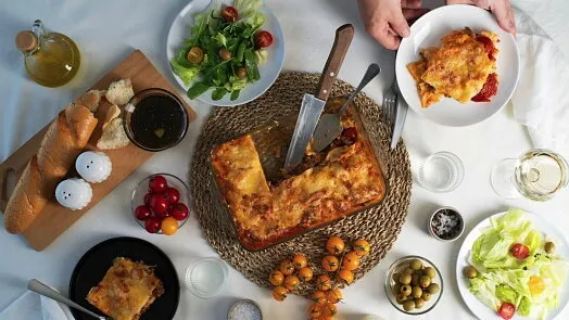 Svěží lasagne s saláty, chlebem a dalšími přílohami na stole.