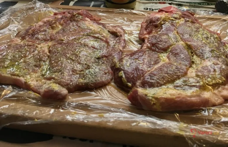 Dvě vepřové krkovice namočené v omáčce na dřevěném prknu.