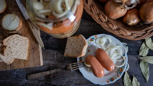 Utopenci recept: nakládané cibule s klobásou na dřevěném stole.