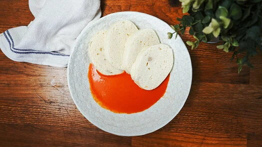 Bílá talíř s červenou rajskou omáčkou a kousky chleba.