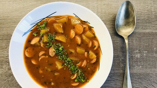 Miska s hotovou frankfurtskou polévkou na dřevěném stole.