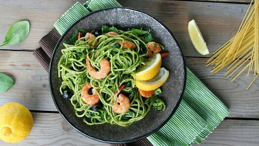 Pasta se špenátem a krevety s citronem na talíři.