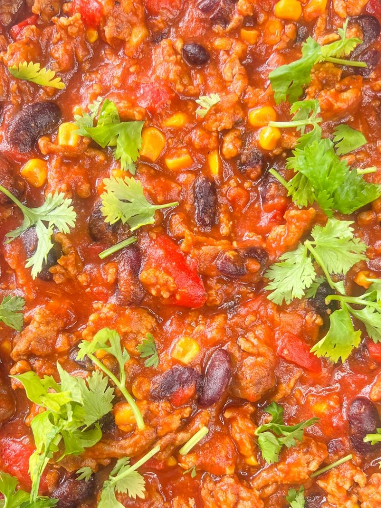 Chilli s mletým masem, fazolemi a kukuřicí ozdobené koriandrem.