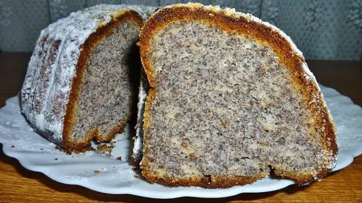 Kousek koláče s makem posypaný moučkovým cukrem na talíři.