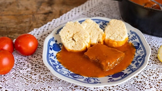 Znojemská omáčka s pečeněmi na talíři vedle rajčat.