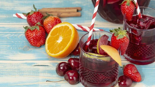 Sklenice s červenou sangrií ozdobená jahodami, pomerančem a višněmi.