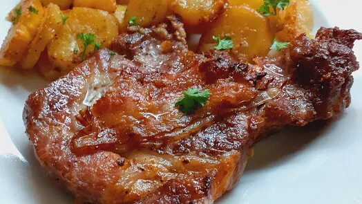 Pečená vepřová krkovice s bramborami na bílém talíři.