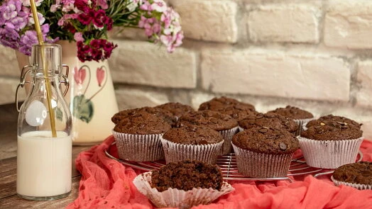 Čokoládové muffiny s čokoládovými kousky, mléko v láhvi a květiny.