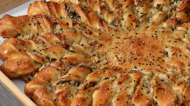 Zlatohnědá plněná pizza šnek s sezamem na dřevěném podnosu.