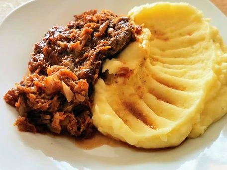 Porce s bramborovou kaší na bílém talíři.