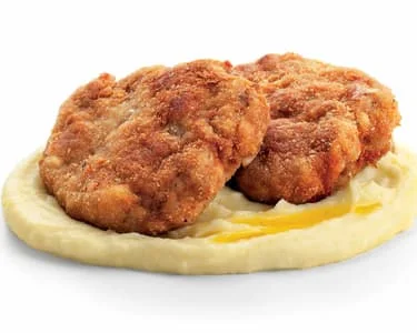 Dva smažené řízkové kotlety na bramborovém pychu.