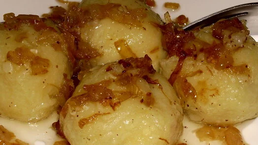 Hot knedlíky s karamelovanou cibulí na bílém talíři.