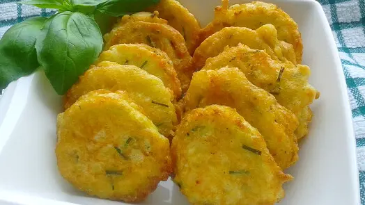 Zlatě opečené cuketové placky na bílém talíři s bazalkou.