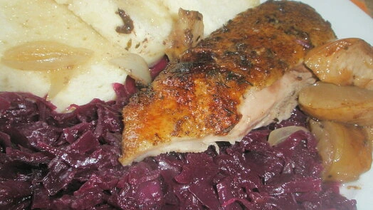 Pečená kachna s červenou kapustou, bramborami a cibulí na talíři.