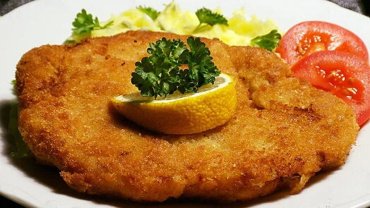 Zlatě hnědý řízek s citronem a petrželkou na bílém talíři.